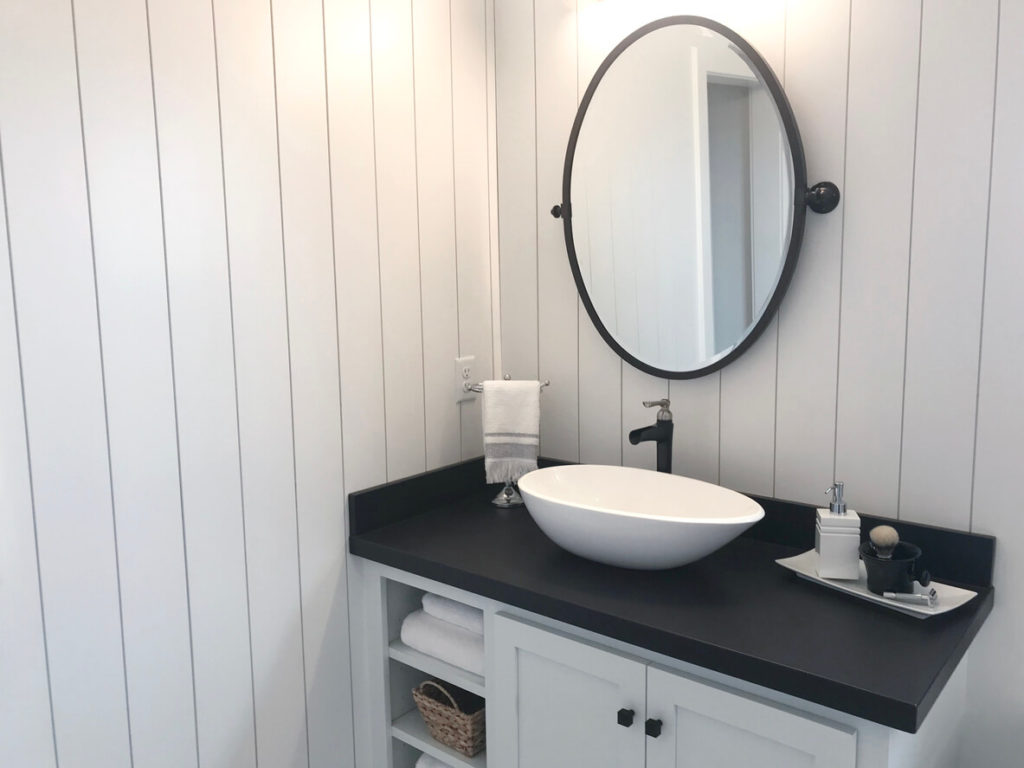 A vanity with a black countertop that matches the faucet, mirror, and handles