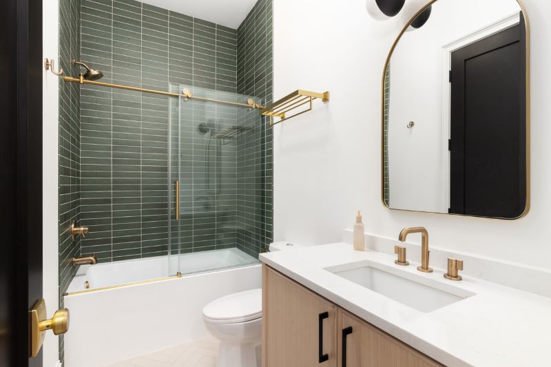 A photo of a bathroom with green tiles surrounding the bathtub, and gold fixtures.
